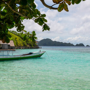 Longboat in a turquoise lagoon framed by leaves, islands beyond, Misool, Raja Ampat, Indonesia