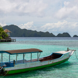 Green and white longboat moored in turquoise lagoon, karst islands behind, Misool, Raja Ampat, Indonesia
