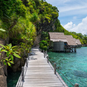 Wooden boardwalk along a cliff leading to thatched bungalows, vertical, Misool, Raja Ampat, Indonesia