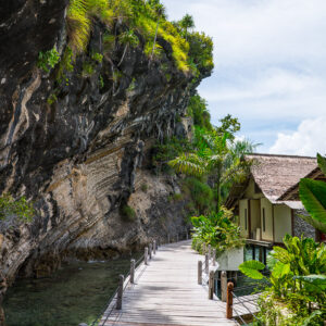 Boardwalk beneath an overhanging limestone cliff to a bungalow, vertical, Misool, Raja Ampat, Indonesia