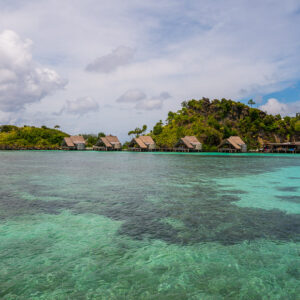 Lagoon reef patches in foreground with distant row of bungalows, Misool, Raja Ampat, Indonesia