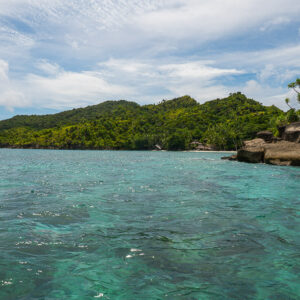 Low forested coastline with dark rocks on the right, Misool, Raja Ampat, Indonesia