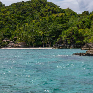 Villas en chaume sur la plage sous la jungle, rochers au premier plan, Misool, Raja Ampat, Indonésie