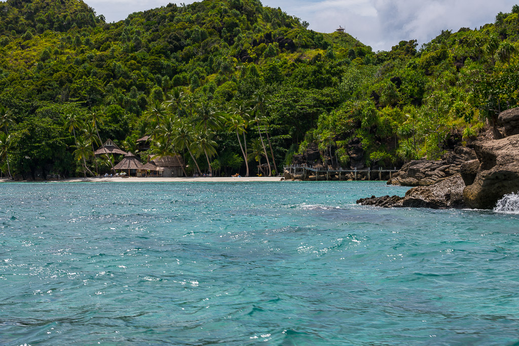 Villas en chaume sur la plage sous la jungle, rochers au premier plan, Misool, Raja Ampat, Indonésie