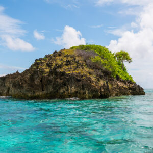 Dark rock islet with a tuft of vegetation and puffy clouds, Misool, Raja Ampat, Indonesia