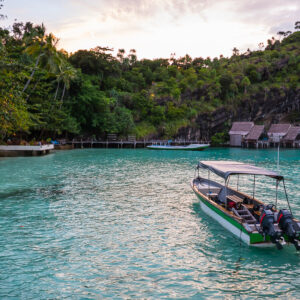 Longboat in a lagoon at dusk with bungalows below a cliff, Misool, Raja Ampat, Indonesia