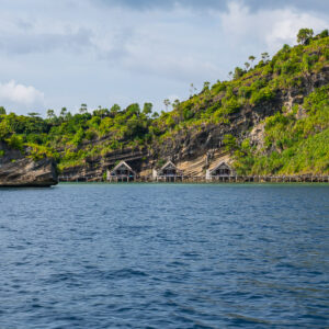 Jungle-covered cliff with a row of bungalows at its foot, Misool, Raja Ampat, Indonesia