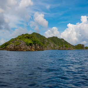 Forested karst islet under towering cumulus clouds, Misool, Raja Ampat, Indonesia