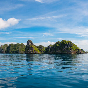 Row of karst islets reflected in calm water, wispy clouds, Misool, Raja Ampat, Indonesia