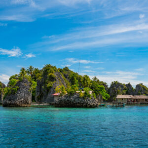 Karst islets with stilt huts at their base under blue sky, Misool, Raja Ampat, Indonesia