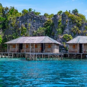 Two thatched stilt huts at the foot of karst cliffs, Misool, Raja Ampat, Indonesia