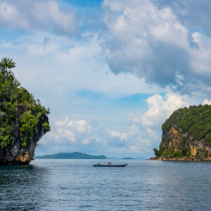 Small boat in a channel between karst islets, vertical, Misool, Raja Ampat, Indonesia