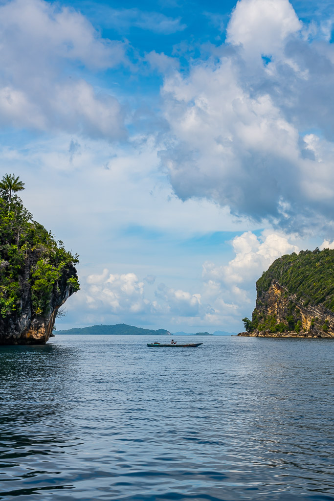 Small boat in a channel between karst islets, vertical, Misool, Raja Ampat, Indonesia