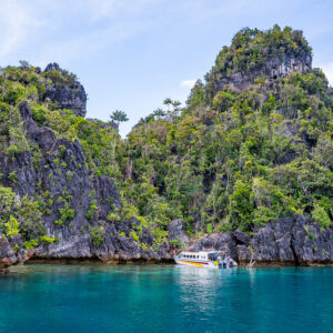 Vedette blanche au pied de hautes falaises karstiques boisées, Misool, Raja Ampat, Indonésie