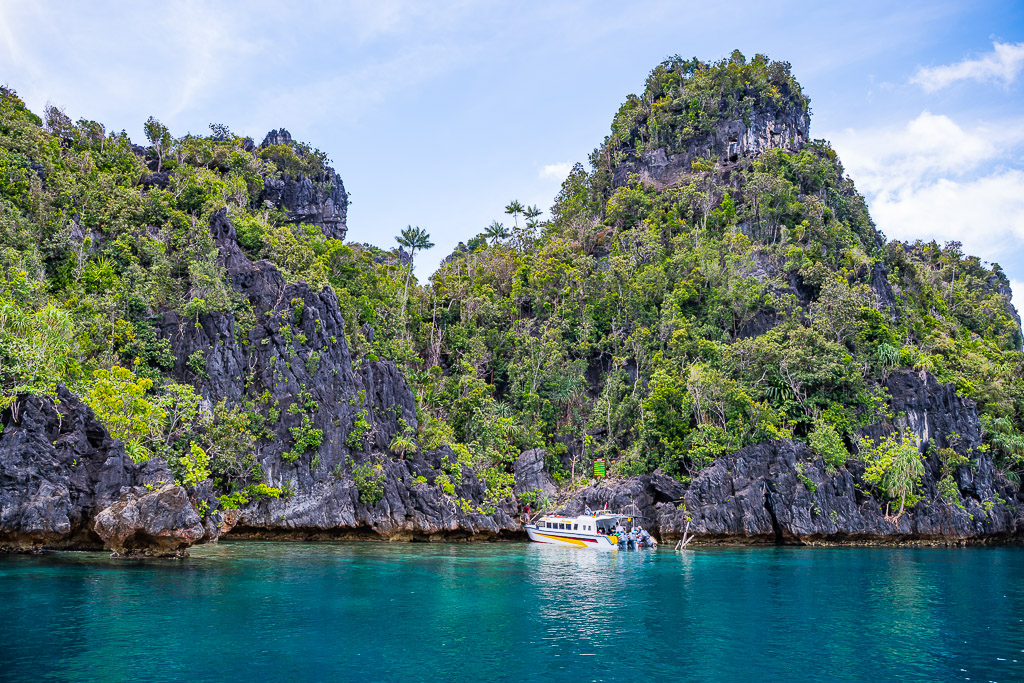 White speedboat at the foot of tall forested karst cliffs, Misool, Raja Ampat, Indonesia