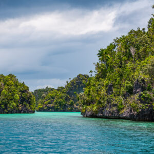 Turquoise channel between jungle-covered karst islands, grey sky, Misool, Raja Ampat, Indonesia