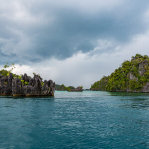Jagged karst islet and forested island under heavy storm clouds, Misool, Raja Ampat, Indonesia