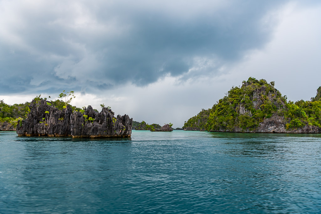 Jagged karst islet and forested island under heavy storm clouds, Misool, Raja Ampat, Indonesia