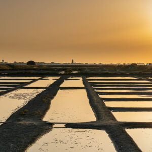 Sun low in hazy golden sky above converging salt pan walkways, Le Croisic, Brittany, France