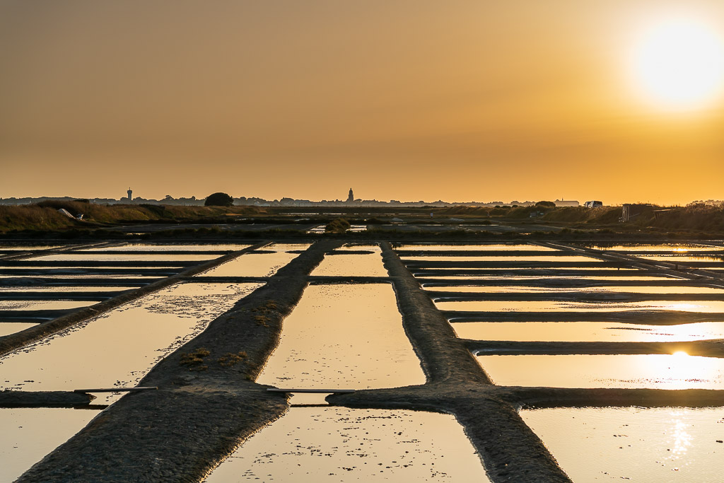 Sun low in hazy golden sky above converging salt pan walkways, Le Croisic, Brittany, France