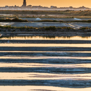 Vertical layered salt pans reflecting golden sky below a distant tower, Le Croisic, Brittany, France