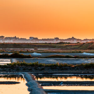 Church tower silhouette against orange sky over salt marsh pools, Le Croisic, Brittany, France