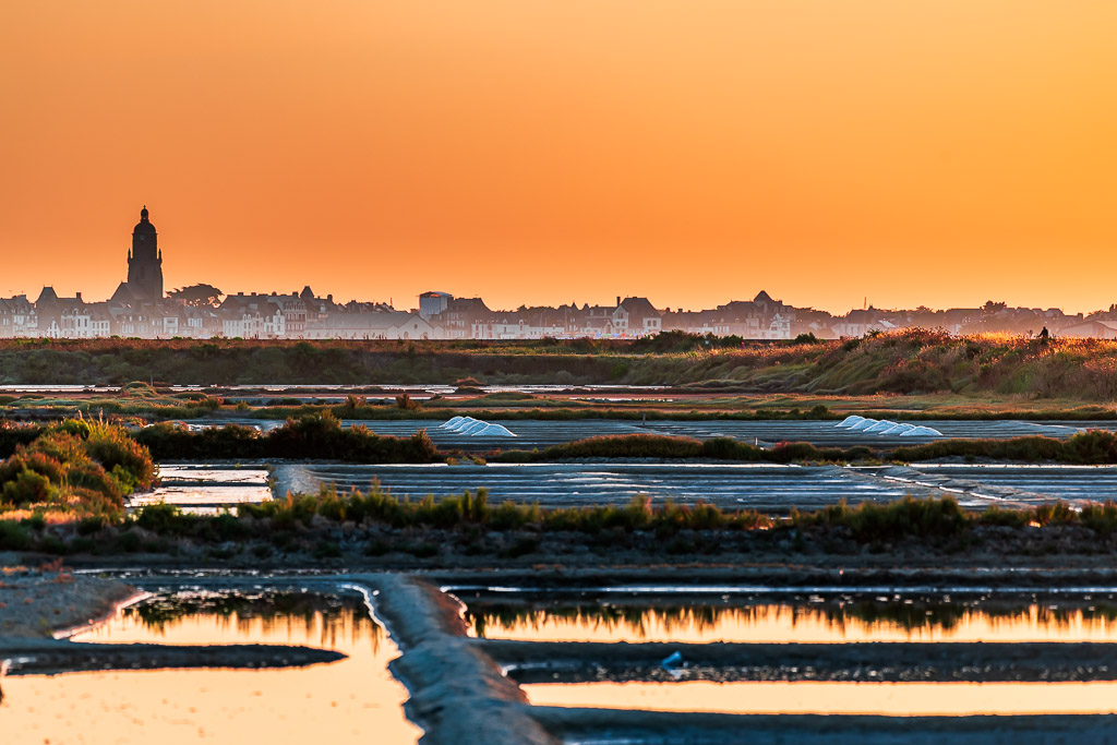 Church tower silhouette against orange sky over salt marsh pools, Le Croisic, Brittany, France