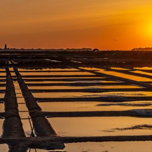 Setting sun over salt pan grid with diagonal walkways and orange sky, Le Croisic, Brittany, France