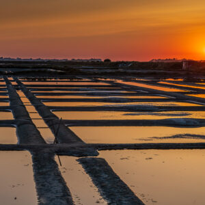 Red sun near the horizon over salt pans with crossing walkways, Le Croisic, Brittany, France