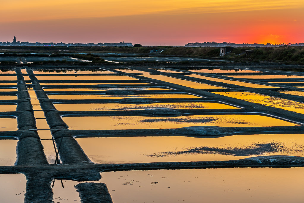 Red afterglow on horizon over salt pan grid reflecting yellow sky, Le Croisic, Brittany, France