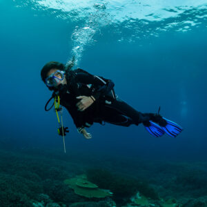 Woman diver posing in blue water above a staghorn coral field, Raja Ampat, Indonesia