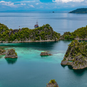 Karst islets with a traditional sailing schooner anchored beyond, Waigeo, Raja Ampat, Indonesia