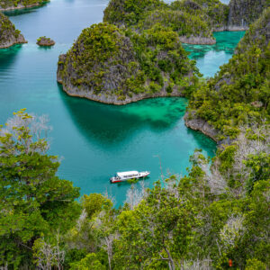 Small boat crossing a narrow channel between karst islets, Waigeo, Raja Ampat, Indonesia