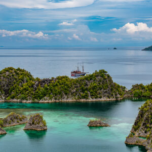 Traditional schooner anchored behind a forested islet, Waigeo, Raja Ampat, Indonesia