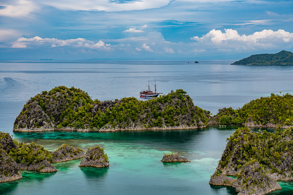 Traditional schooner anchored behind a forested islet, Waigeo, Raja Ampat, Indonesia