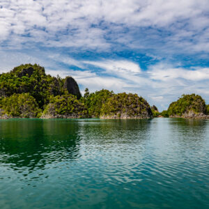 Forested karst islands reflected in a calm green lagoon, Raja Ampat, Indonesia
