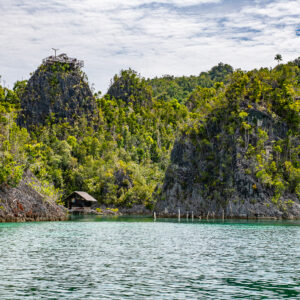 Karst cliffs and stilt hut at the edge of a calm lagoon, Raja Ampat, Indonesia