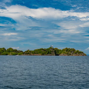 Low forested island on the horizon under a cloudy sky, Raja Ampat, Indonesia