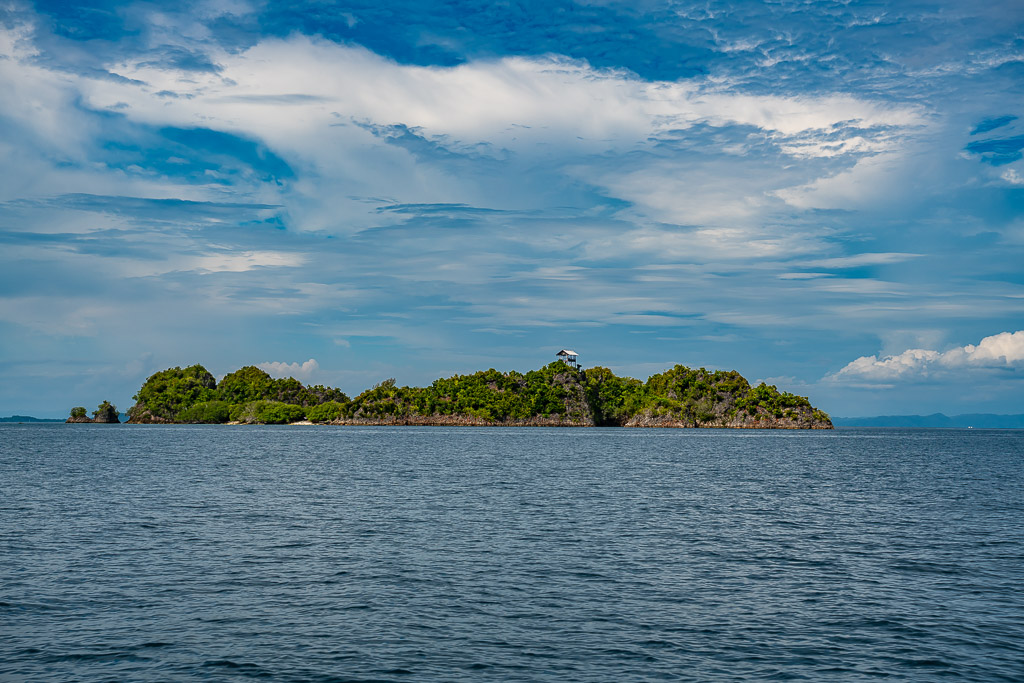 Low forested island on the horizon under a cloudy sky, Raja Ampat, Indonesia