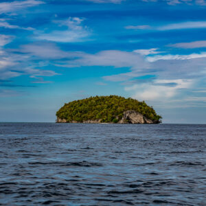 Small forested island alone on open sea under a blue cloudy sky, Raja Ampat, Indonesia