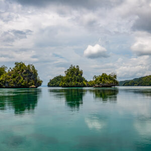 Mushroom islets and wooded shore reflected under a cloudy sky, Waigeo, Raja Ampat, Indonesia