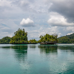 Three small islets in a calm lagoon under a grey cloudy sky, Waigeo, Raja Ampat, Indonesia