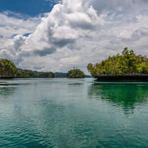 Distant islets reflected on a glassy lagoon beside a cliff, Waigeo, Raja Ampat, Indonesia