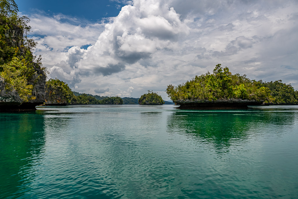 Distant islets reflected on a glassy lagoon beside a cliff, Waigeo, Raja Ampat, Indonesia