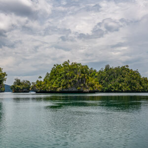Forested islets reflected on still water under a hazy sky, Waigeo, Raja Ampat, Indonesia