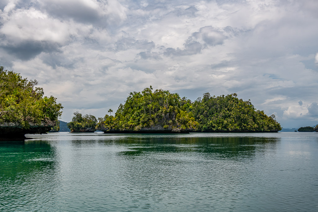 Forested islets reflected on still water under a hazy sky, Waigeo, Raja Ampat, Indonesia