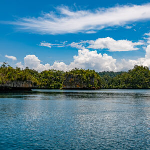 Line of low forested islets under a blue sky with wispy clouds, Waigeo, Raja Ampat, Indonesia