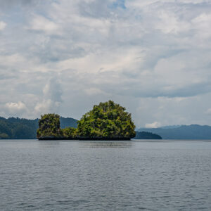 Two islets before a mountainous coastline under grey clouds, Waigeo, Raja Ampat, Indonesia