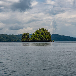 Small rocky islet alone in a wide bay under heavy clouds, Waigeo, Raja Ampat, Indonesia