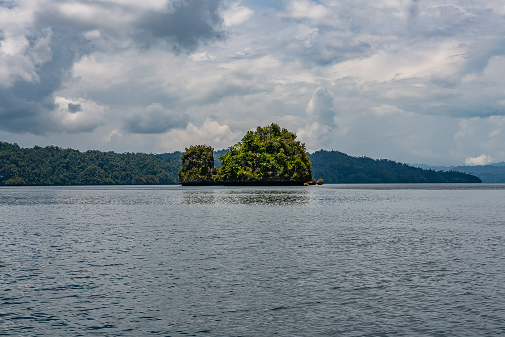 Small rocky islet alone in a wide bay under heavy clouds, Waigeo, Raja Ampat, Indonesia